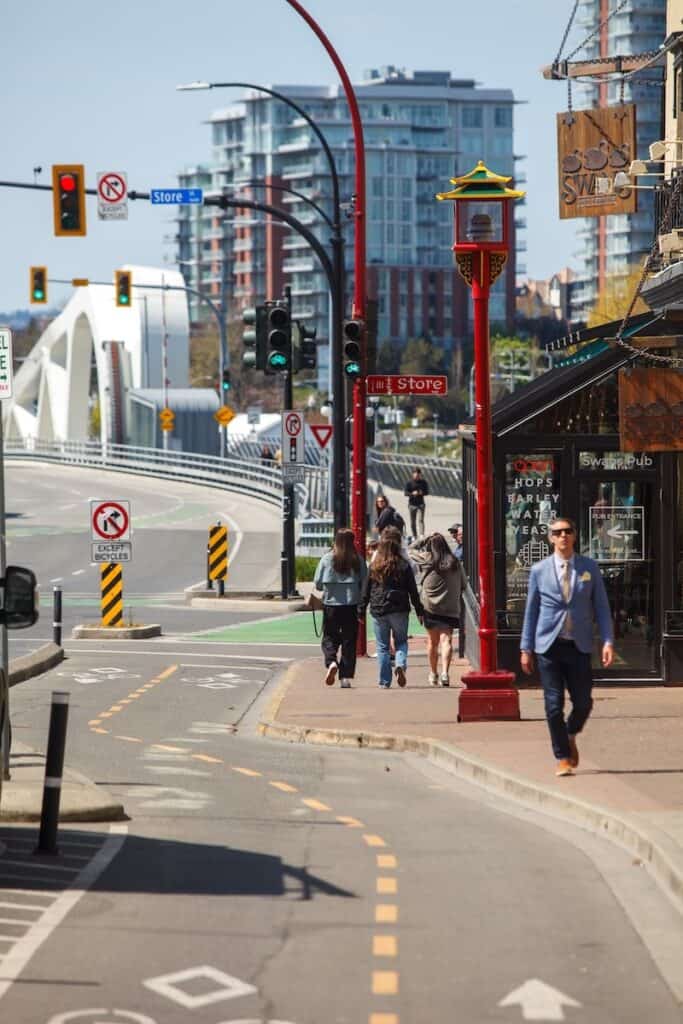 pedestrians on the sidewalk with the johnson street bridge in the background